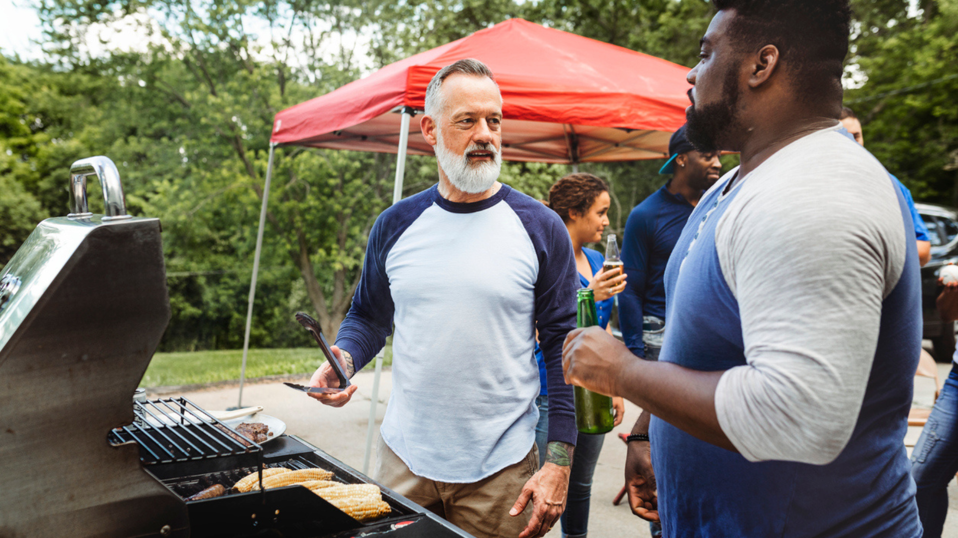 A man at a tailgate grills while talking to a friend who is drinking a beverage before a game of football in North Carolina