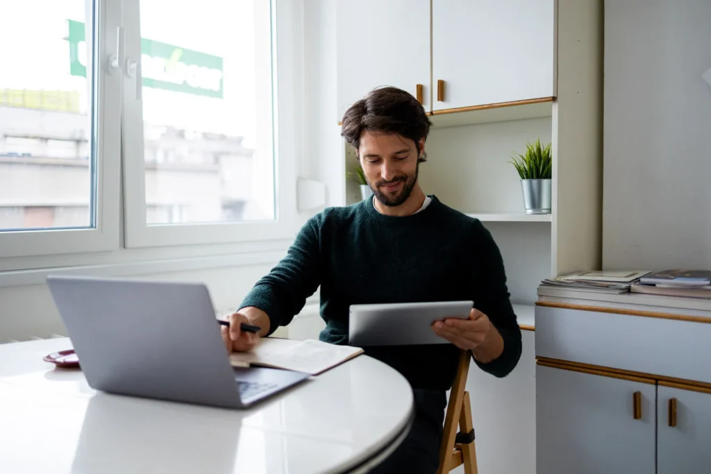 A man looks at papers while working on his laptop so he can sell a home fast