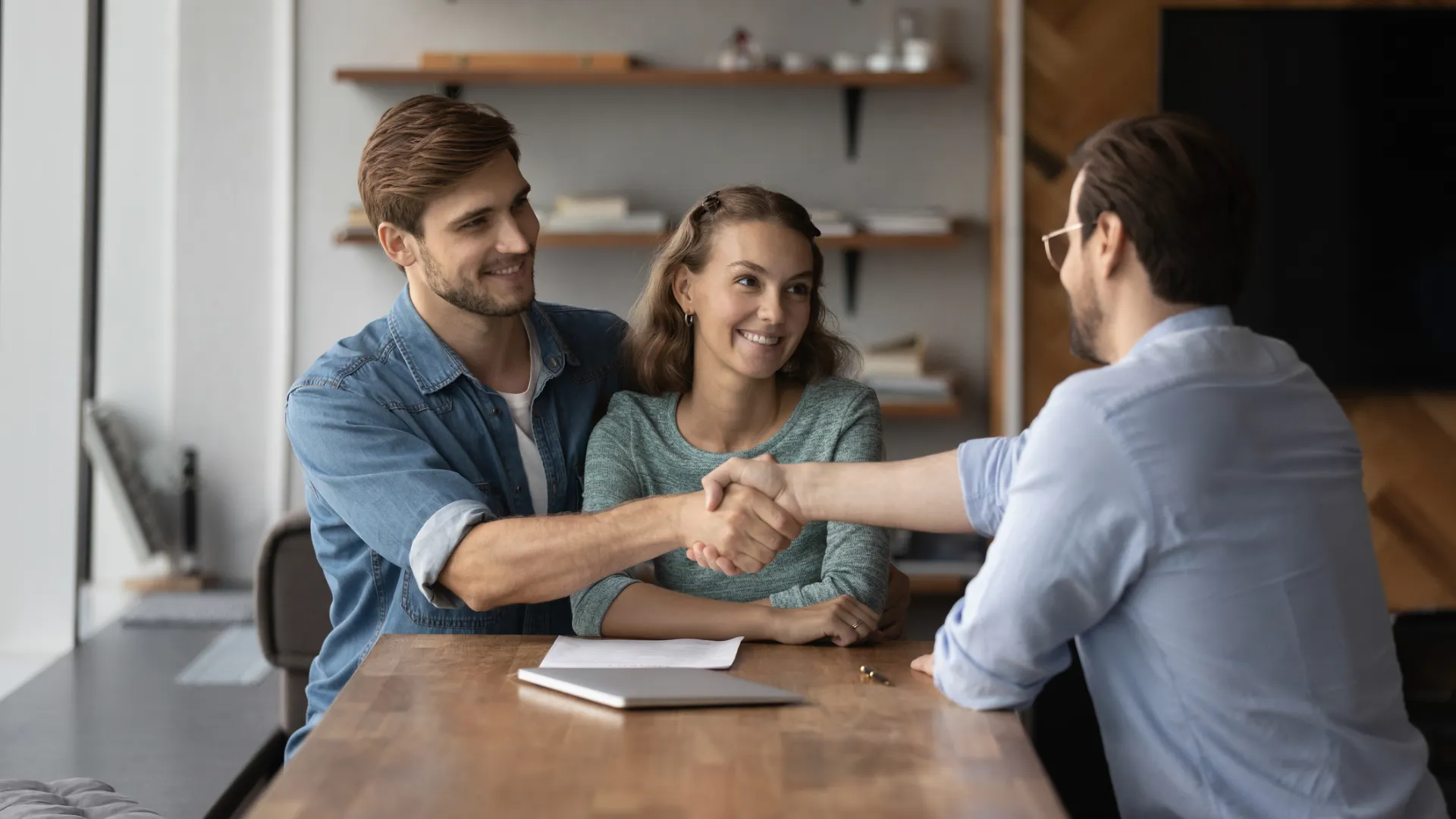 A couple smile at an agent, who is shaking hands with the husband after they learned about selling a home with a lien against it