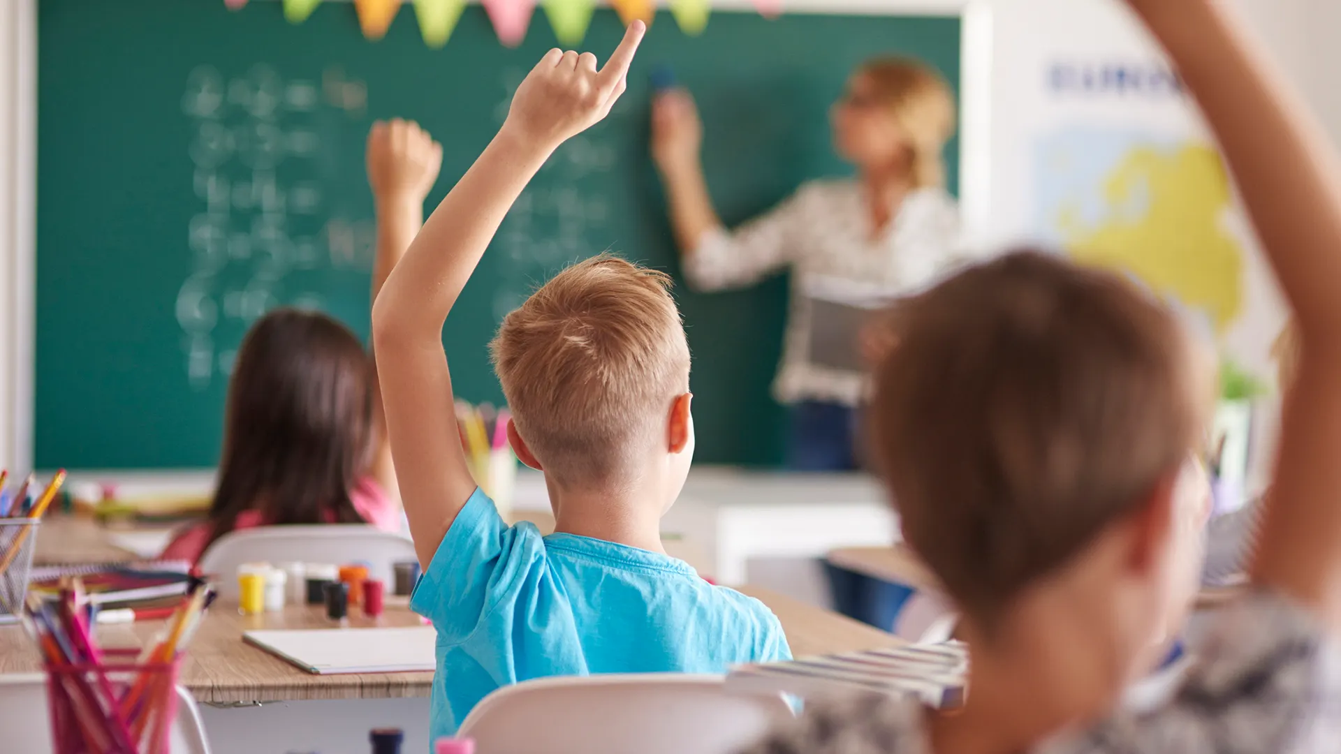 Elementary school students raise hands in a classroom at one of the schools in the Triangle