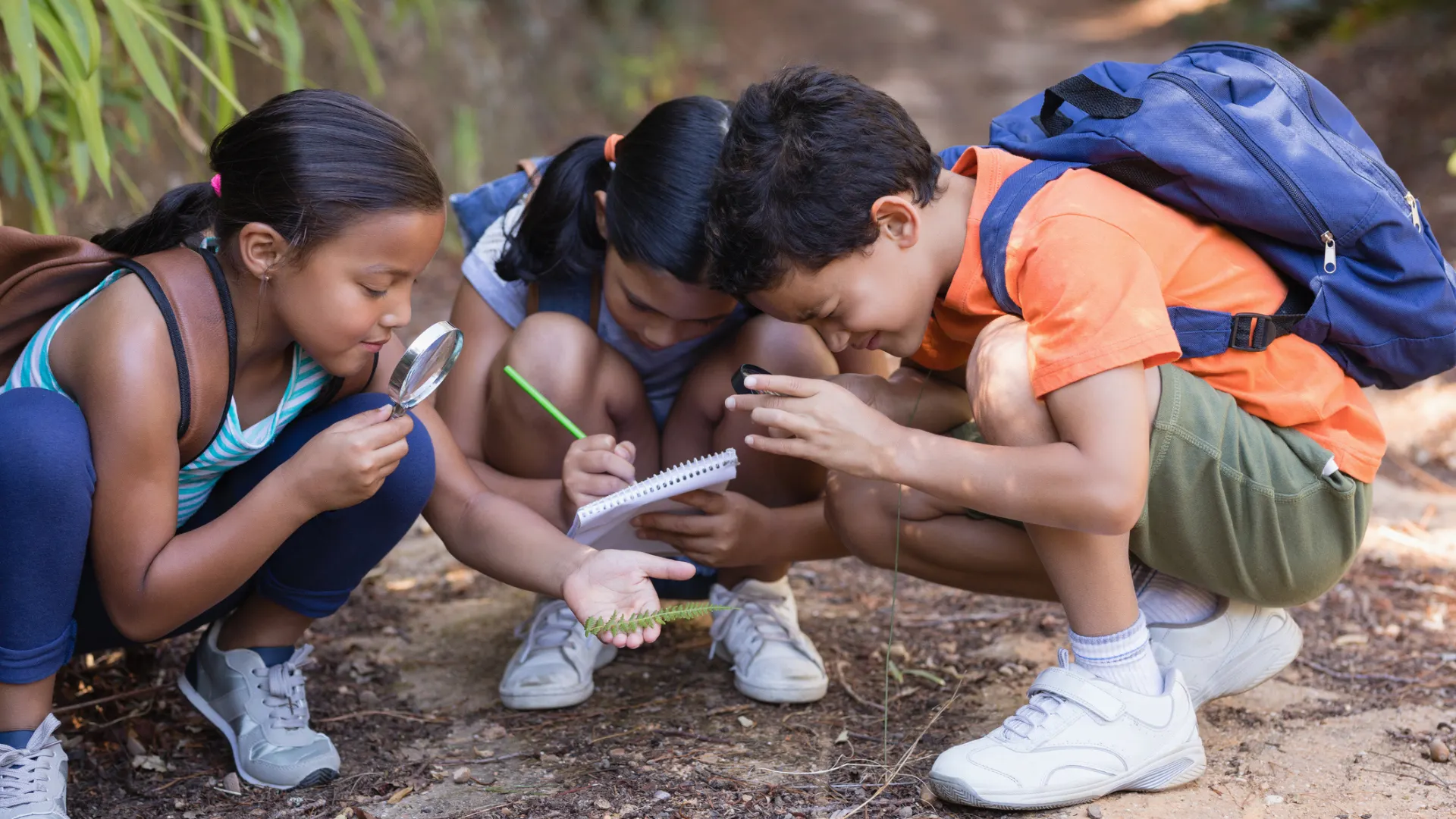 Three kids explore and take notes in nature. Outdoor activities are some of the late summer activities for families that you can enjoy.