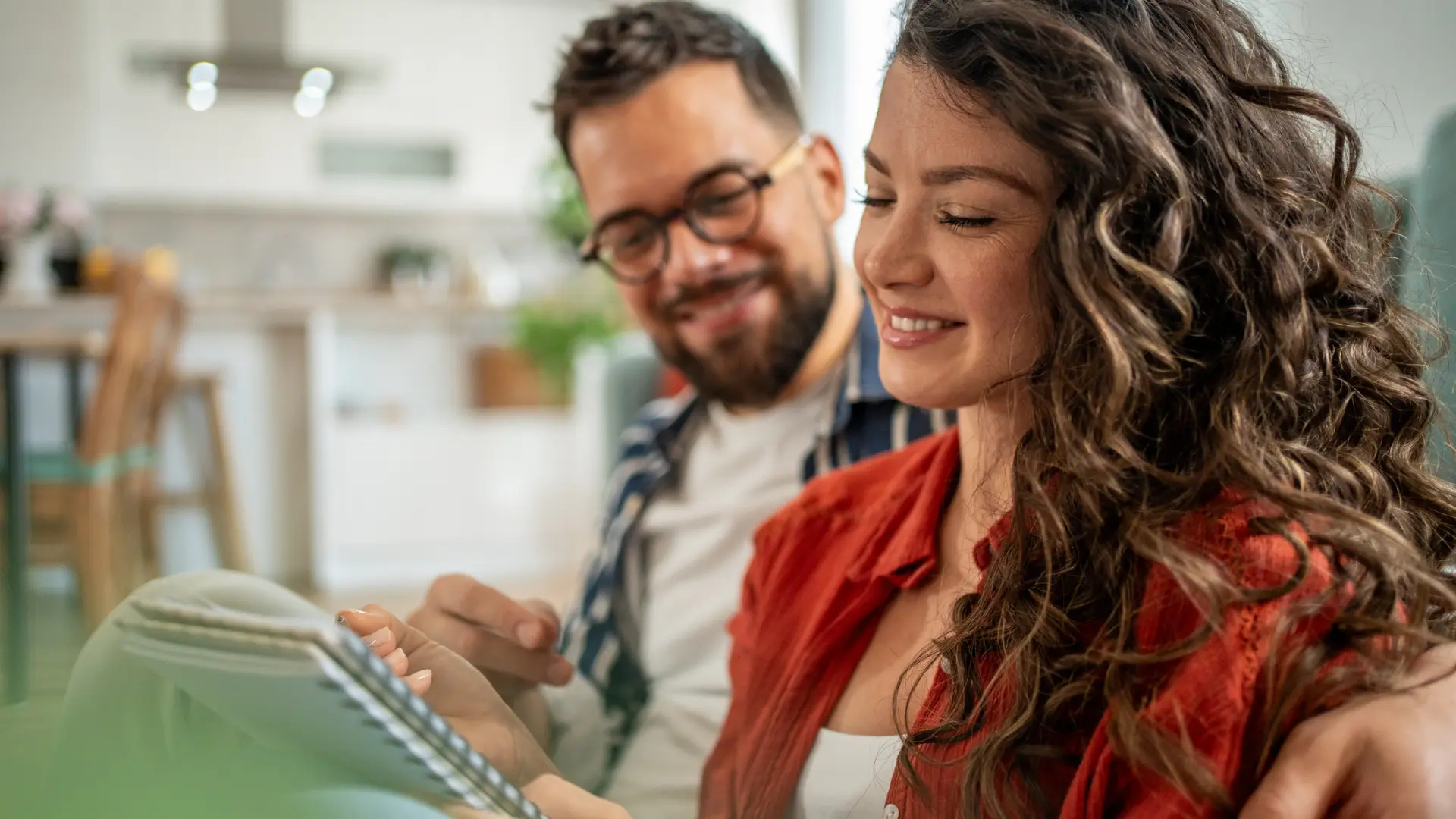A husband and wife sit on a couch smiling while working on a budget to determine if current Triangle mortgage rates will help them buy a home