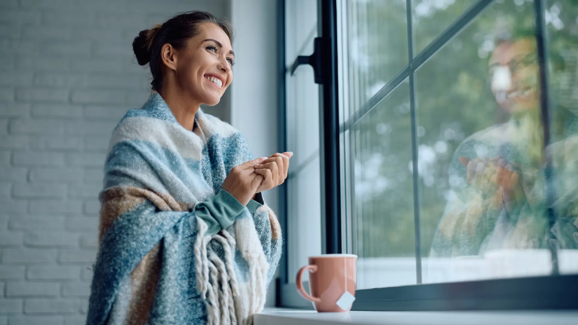 A happy woman smiles and looks out of her window on a cold day after completing her 10-step winter home maintenance checklist for North Carolina homeowners