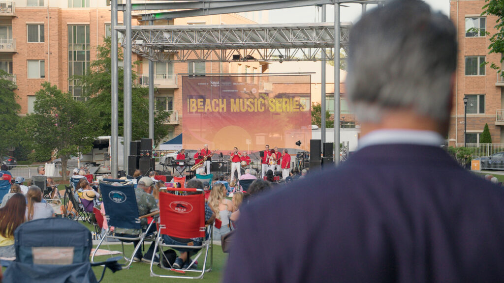A man stands watching a band playing during the Beach Music Series in Raleigh's North Hills district.