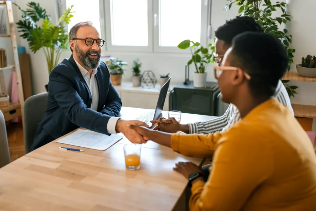 A mortgage lender shakes hands with a couple who are discussing whether a construction loan or traditional mortgage is right for you.